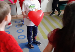 Dzieci bawią się w kole z czerwonym balonem w kształcie serca.