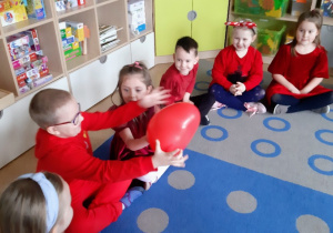 Dzieci siedząc w kole przekazują sobie balona w kształcie serca.