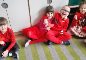 Dzieci ubrane na czerwono trzymają czerwone serduszka.