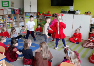 Dzieci tańczą przy muzyce w środku koła utworzonego przez siedzące dzieci.