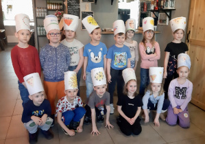 Dzieci pozują do zdjęcia grupowego w samodzielnie wykonanych czapkach kucharskich.