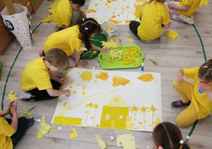 Dzieci w dwóch zespołach przyklejają żółte materiały na białe brystole.