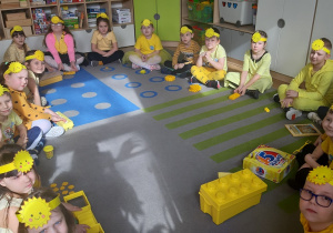 Dzieci siedzące w kole mają przed sobą przedmioty w kolorze żółtym.