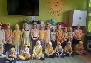 Dzieci ustawione w dwóch rzędach prezentują wykonane przez siebie opaski na głowę z emblematem słońca.