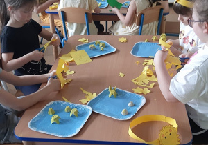 Dzieci siedzące przy stolikach wykonują pracę plastyczno - techniczną pt. Żółte żonkile.