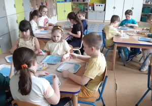 Dzieci siedzące przy stolikach malują papierowe talerzyki farbą plakatową.