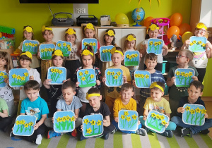 Dzieci ustawione w trzech rzędach prezentują wykonane przez siebie prace pt. Żółte żonkile.