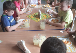 Dzieci degustują sałatkę z żółtych owoców i lemoniadę cytrynową.