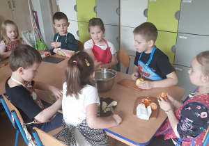 Dzieci przygotowują sałatkę z owoców w kolorze żółtym.