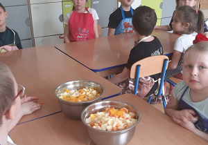 Dzieci przygotowują sałatkę z owoców w kolorze żółtym.