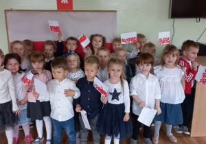 Dzieci z własnoręcznie wykonanymi flagami Polski pozują na tle dekoracji