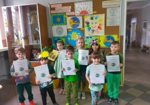 Dzieci z nagrodami za udział w konkursie "Promyczkowe logo" na tle prac konkursowych