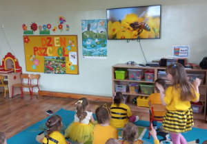 Dzieci siedzą przed ekranem telewizora i ogladają film edukacyjny o życiu pszczół i ich znaczeniu dla naszej planety