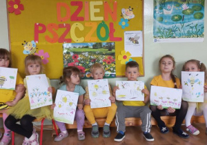 Dzieci prezentują swoje prace przedstawiające pszczoły na tle dekoracji