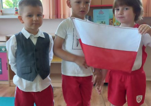 Kuba, Antek i Jaś prezentują biało - czerwone stroje trzymając flagę