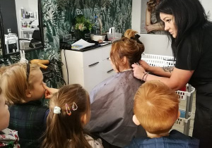 Pani fryzjerka pokazuje dzieciom jak wygląda jej praca w praktyce.