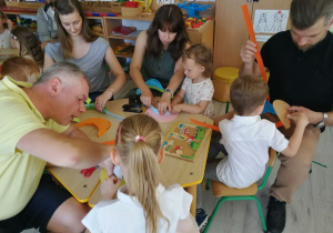 Dzieci wspólnie z rodzicami robią daszki z kartonów.