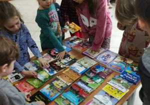 Dzieci oglądają książki ułożone na stoliku.