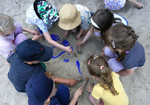 Dzieci w piaskownicy szukają szkieletu dinozaura.
