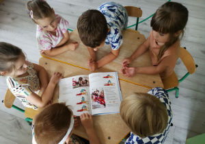 Dzieci przy stoliku oglądają książkę o pierwszej pomocy.
