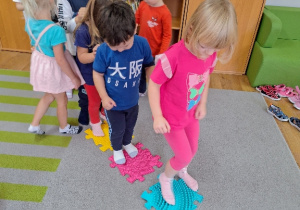 Dzieci boso przechodzą po ścieżce ułożonej z puzzli sensorycznych.