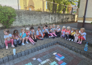Dzieci piją wodę z kubeczków na placu zabaw.