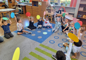 Dzieci siedzą w kole i biorą udział w zabawie dydaktycznej "Podnieś kropkę".