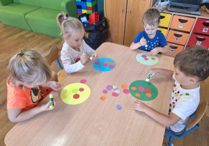 Dzieci wykonują przy stolikach pracę plastyczną pt. "Piłka w kolorowe kropki".