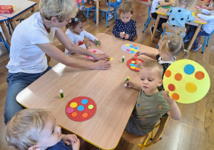 Dzieci wykonują przy stolikach pracę plastyczną pt. "Piłka w kolorowe kropki".