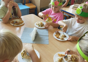 Dzieci jedzą pieczone jabłka przy stolikach