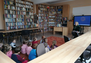 Dzieci siedzą na dywanie przed panią z biblioteki.