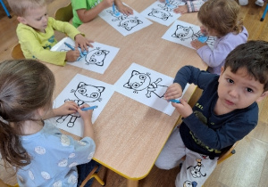 Dzieci kolorują przy stolikach postać Kici Koci.