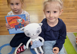 Klara i Zosia prezentują maskotkę Kici Koci oraz książeczkę pt. "Kicia Kocia w przedszkolu".