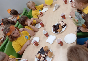 Dzieci siedzą przy stolikach i jedzą słodki poczęstunek