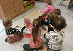 Dzieci oklejają karton sylwetami owoców.