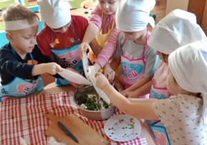 Dzieci wrzucają do miseczki posiekaną zieleninę.