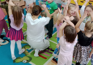 Grupa dzieci wraz z prowadzącą machają rękoma ponad głowami.