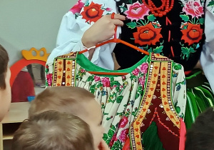 Tancerka prezentuje dzieciom damski strój krakowski.