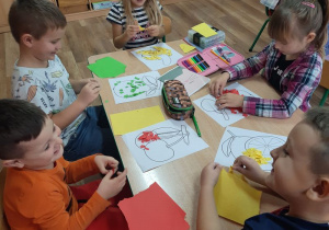 Dzieci wyklejają kolorowymi papierkami obrazki konturowe przedstawiające owoce