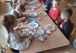 Dzieci siedzą przy stole i dekorują pierniczki