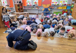 Dzieci ćwiczą wspólnie z policjantem bezpieczną pozycję pieska.