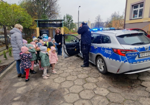 Policjant prezentuje dzieciom pojazd policyjny.