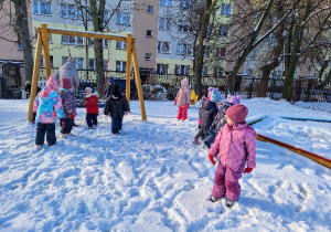 Dzieci bawią się w ogrodzie przedszkolnym na śniegu.