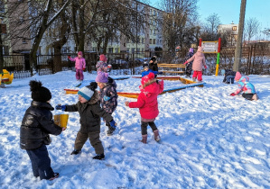 Dzieci bawią się w ogrodzie przedszkolnym na śniegu.