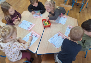 Dzieci wykonują przy stoliku zimowe karty pracy.