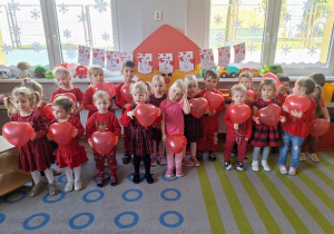 Dzieci pozują do zdjęcia grupowego z czerwonymi balonami w kształcie serduszek..