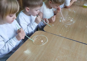 Dzieci dmuchają przy stolikach bańki mydlane