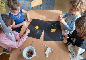 Dzieci siedzą przy stolikach i tworzą Ukłąd Słoneczny z plasteliny