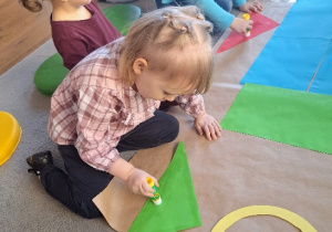 Dzieci przyklejają klejem elementy rakiety do dużego arkusza papieru.