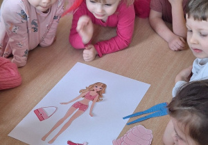 Dzieci "ubierają" lalkę Barbie.